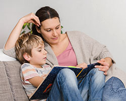 Mutter und Kind sitzen auf dem Sofa und lesen bzw. lernen in einem Buch.