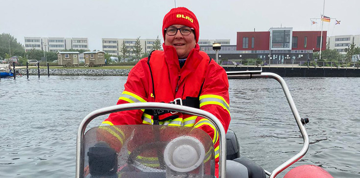 Eine Frau in roter DLRG-Bekleidung sitzt auf einem Boot im Wasser.