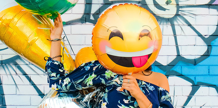 Eine Frau hält Luftballons in der Hand. Ein smily-Luftballon ist direkt vor ihrem Gesicht.