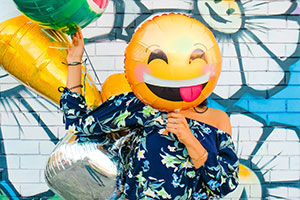 Eine Frau hält Luftballons in der Hand. Ein smily-Luftballon ist direkt vor ihrem Gesicht.