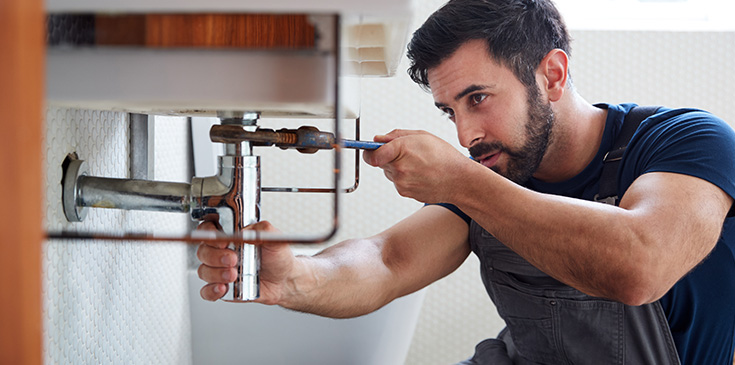 Ein junger Handwerker befestigt einen Waschbecken-Abfluss in einem Badezimmer. 