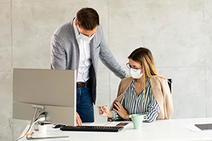 Eine Frau sitzt am Arbeitsplatz. Ihr Kollege schaut ihr über die Schulter und sie besprechen Unterlagen.