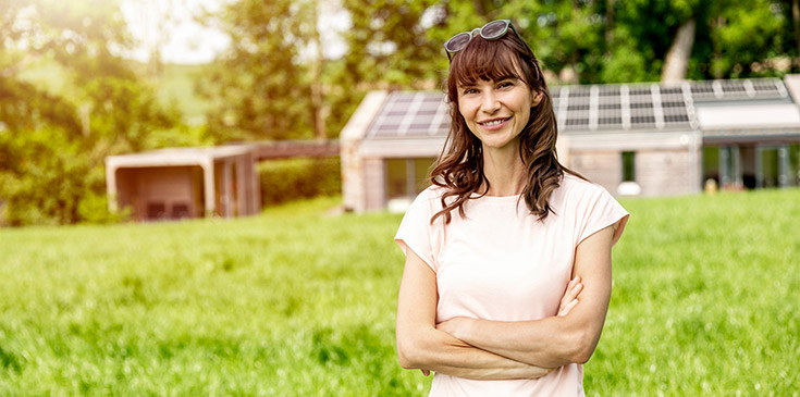 Eine junge Frau steht im Garten vor einer Photovoltaikanlage