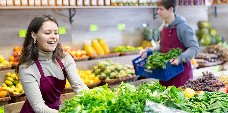 Eine junge Frau mit braunen Haaren räumt die Gemüseregale im Supermarkt ein.