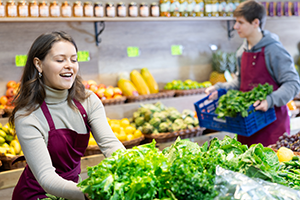 Eine junge Frau mit braunen Haaren räumt die Gemüseregale im Supermarkt ein.