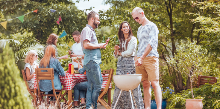 Eine Gruppe junger Menschen feiert ein Sommerfest. Sie grillen auf einer Wiese. 