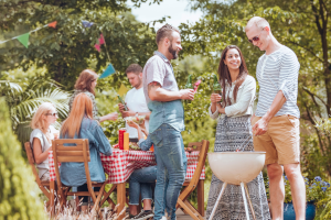 Eine Gruppe junger Menschen feiert ein Sommerfest. Sie grillen auf einer Wiese. 