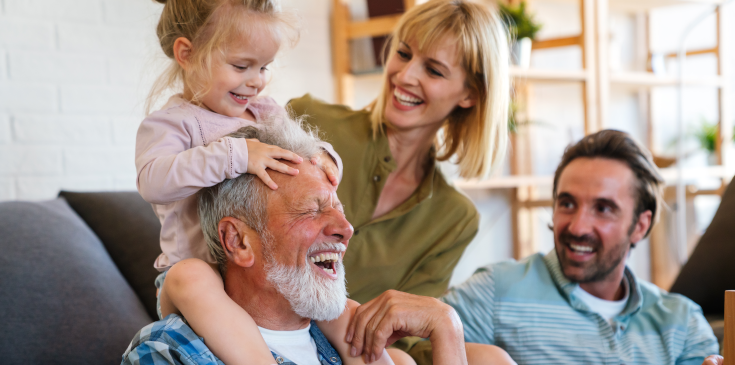 Eine Familie sitzt im Wohnzimmer zusammen und lacht.