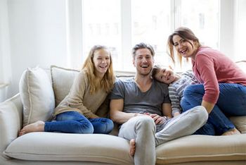 Eine Familie mit zwei Kindern sitzt gemeinsam auf dem Sofa. 