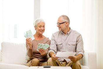 Ein Paar sitzt auf dem Sofa mit Unterlagen und Geld in der Hand.