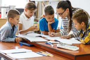 Lehrerin sitzt mit ein paar Schulkindern über Aufgaben.